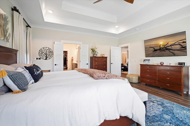 bedroom featuring ceiling fan, dark hardwood / wood-style floors, connected bathroom, a tray ceiling, and ornamental molding