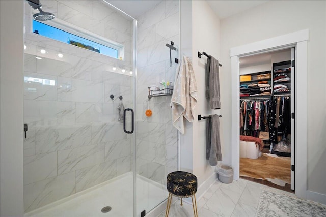 full bath with marble look tiles, a shower stall, a spacious closet, and baseboards