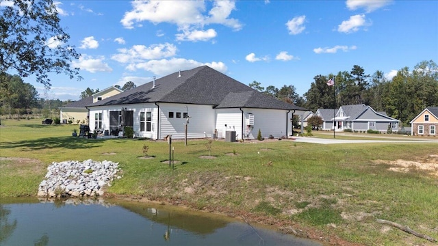 back of house featuring a yard, roof with shingles, cooling unit, and a water view