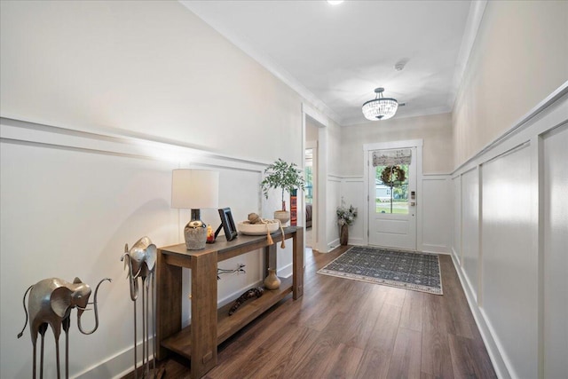 foyer entrance featuring dark wood-type flooring, ornamental molding, and an inviting chandelier