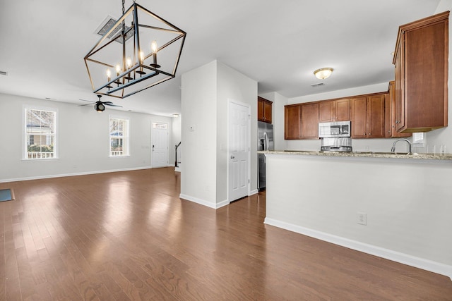 kitchen with stainless steel appliances, light stone countertops, dark hardwood / wood-style flooring, pendant lighting, and sink