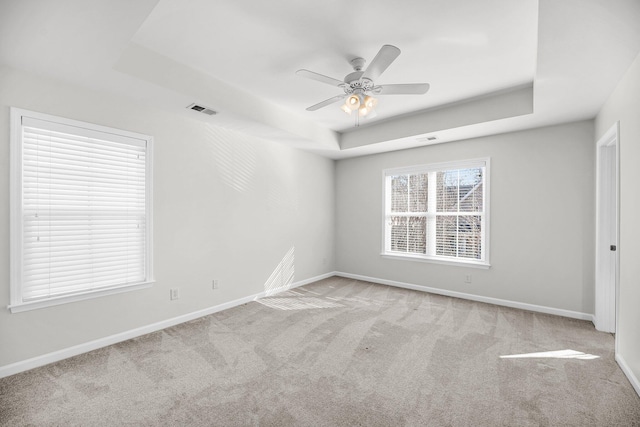 carpeted empty room with a raised ceiling and ceiling fan