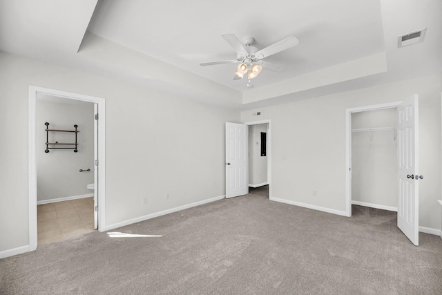 unfurnished bedroom featuring ensuite bath, a raised ceiling, a closet, light colored carpet, and ceiling fan