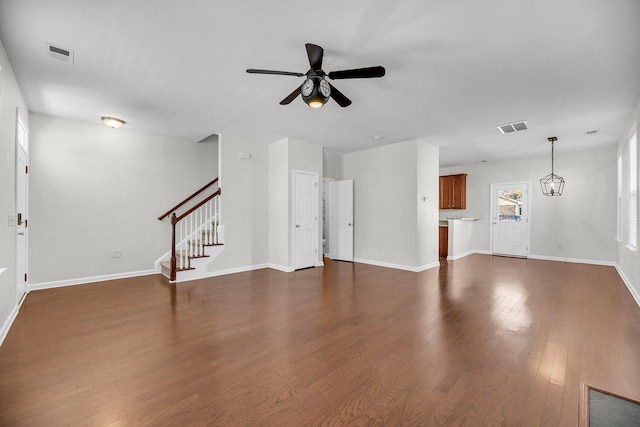 unfurnished living room featuring ceiling fan with notable chandelier and dark wood-type flooring