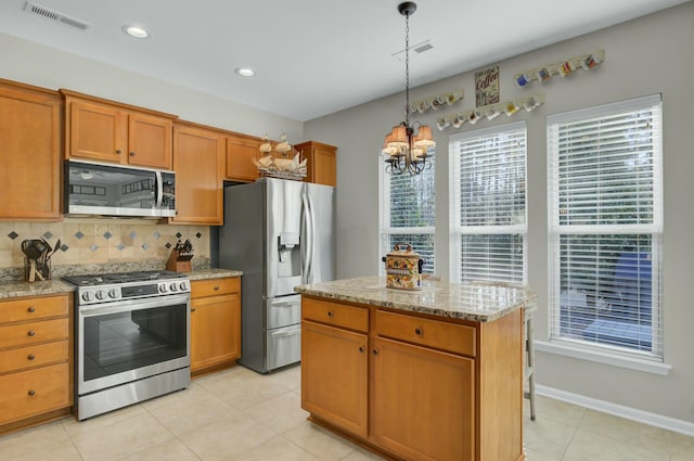 kitchen featuring hanging light fixtures, a kitchen island, stainless steel appliances, light stone countertops, and backsplash