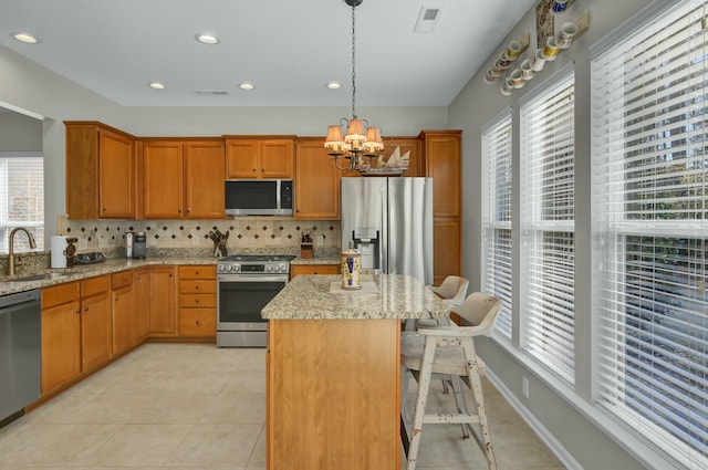 kitchen featuring appliances with stainless steel finishes, pendant lighting, sink, a notable chandelier, and light stone counters