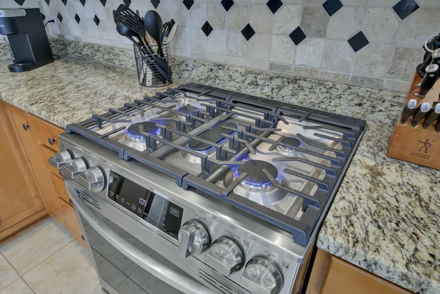 room details featuring stainless steel range with gas cooktop, light stone countertops, and decorative backsplash