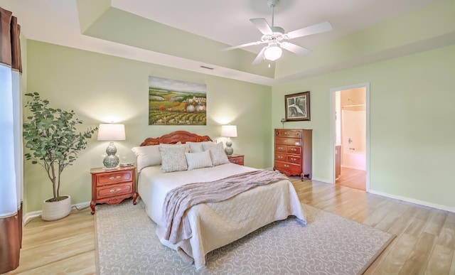 5347 Sundial Ct, North Charleston, SC 29418 - bedroom with light wood-style flooring, a tray ceiling, baseboards, ensuite bath, and a ceiling fan