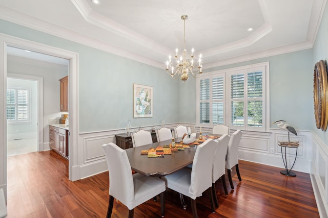 dining area with dark wood-style floors, crown molding, a raised ceiling, and a wainscoted wall