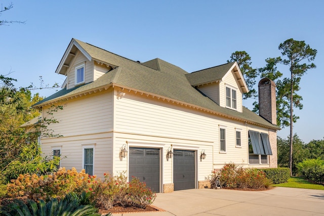 view of home's exterior featuring a shingled roof, a chimney, and concrete driveway