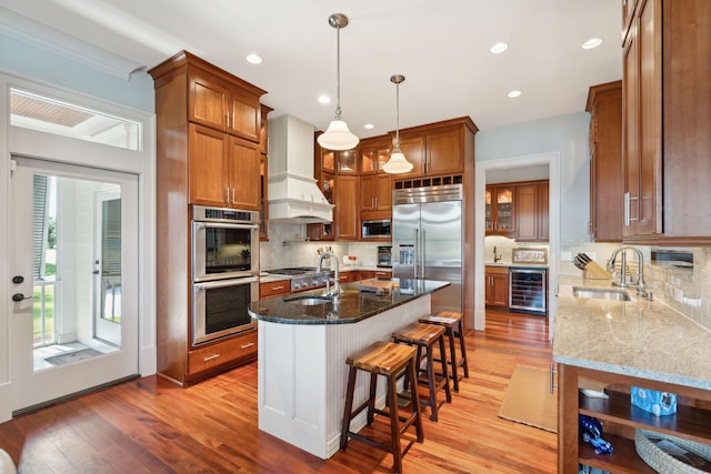 kitchen featuring brown cabinets, stainless steel appliances, a sink, dark stone countertops, and beverage cooler