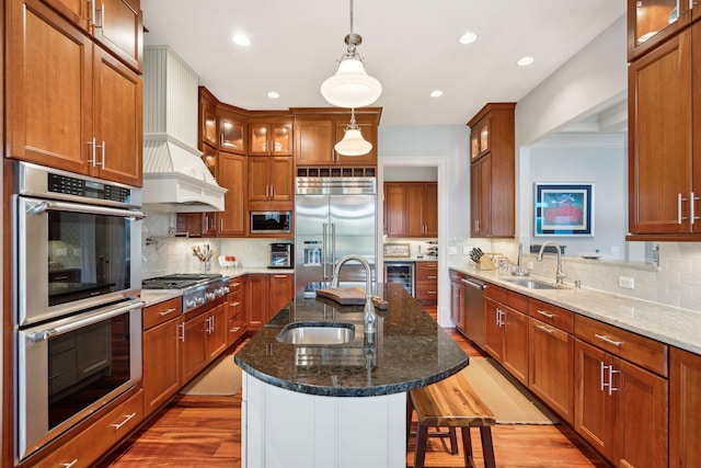 kitchen with glass insert cabinets, dark stone countertops, built in appliances, a kitchen island with sink, and a sink