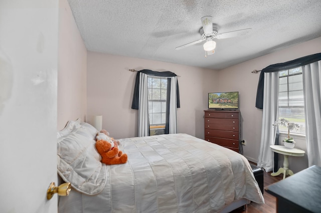 bedroom featuring ceiling fan, a textured ceiling, multiple windows, and dark hardwood / wood-style floors