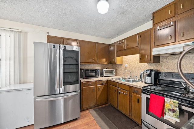 kitchen with sink, light wood-type flooring, appliances with stainless steel finishes, a textured ceiling, and tasteful backsplash