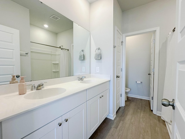 full bathroom featuring double vanity, visible vents, toilet, a sink, and wood finished floors