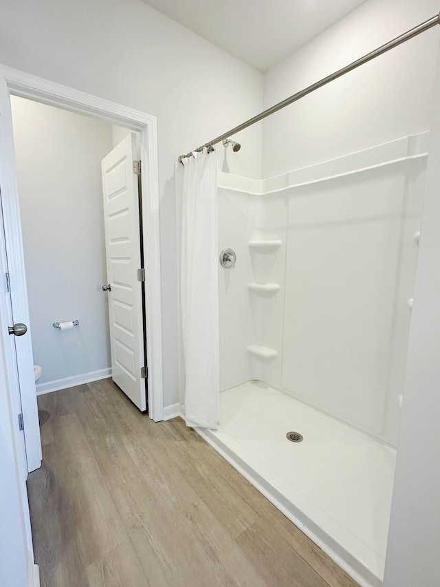 full bath featuring a stall shower, baseboards, and wood finished floors