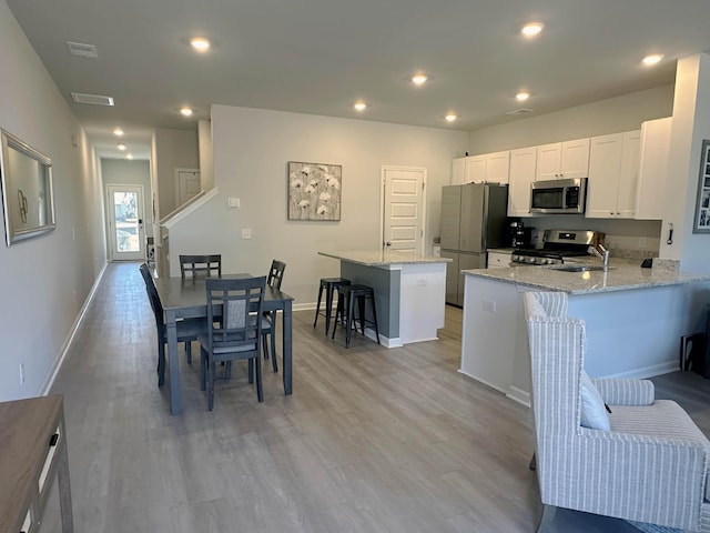 kitchen featuring a breakfast bar area, stainless steel appliances, light stone counters, white cabinets, and kitchen peninsula