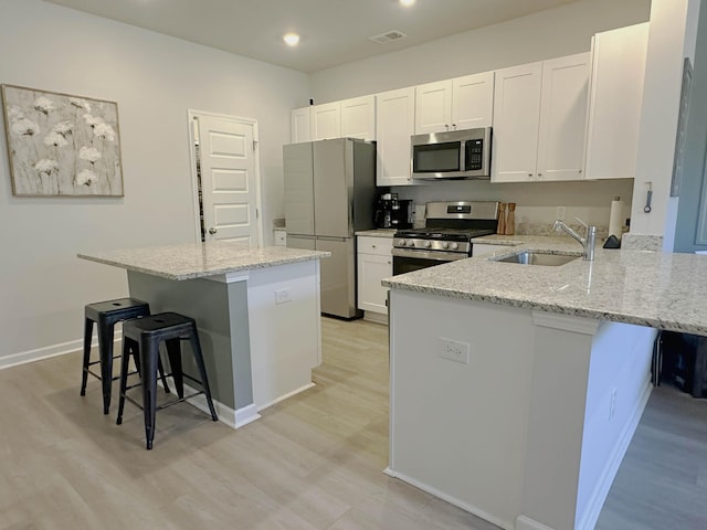 kitchen with stainless steel appliances, a breakfast bar, a peninsula, a sink, and light stone countertops