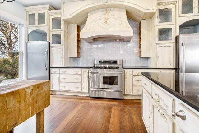 kitchen featuring decorative backsplash, dark hardwood / wood-style flooring, custom range hood, and appliances with stainless steel finishes