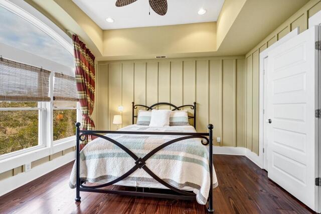 bedroom with dark hardwood / wood-style floors, ceiling fan, and a tray ceiling