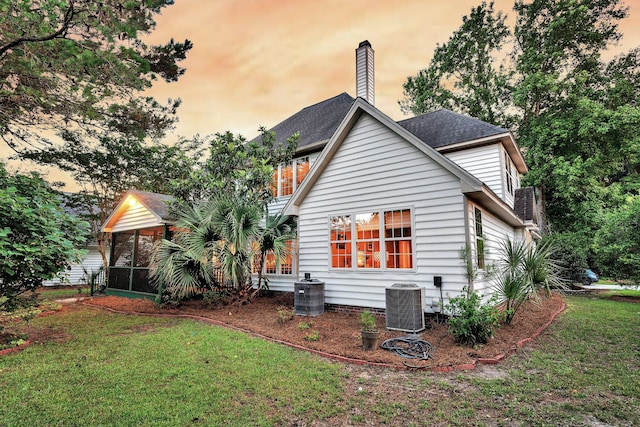 1311 Royal Links Dr, Mount Pleasant, SC 29466 - back of property at dusk with a sunroom, a lawn, a chimney, and a shingled roof
