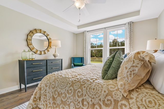 bedroom featuring a ceiling fan, a raised ceiling, wood finished floors, and baseboards