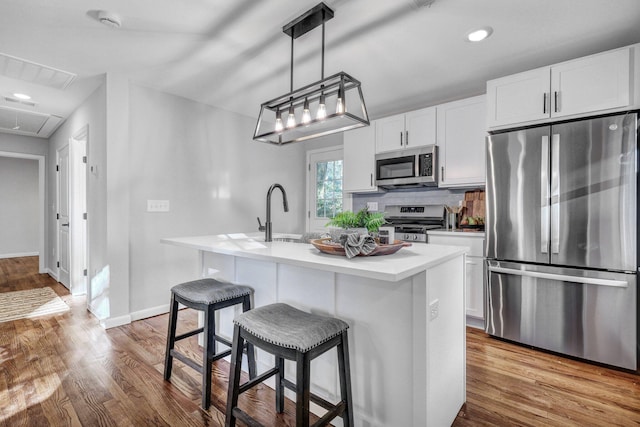 kitchen featuring an island with sink, a sink, wood finished floors, white cabinetry, and stainless steel appliances