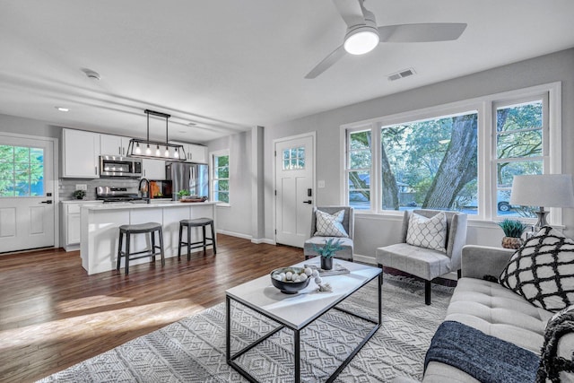 living room featuring visible vents, plenty of natural light, ceiling fan, and dark wood-style flooring