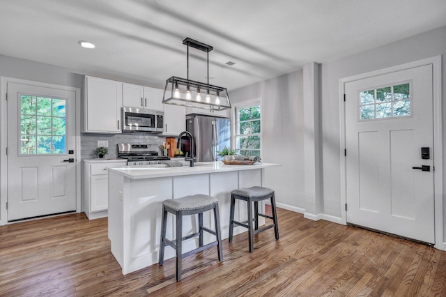 kitchen with a kitchen bar, backsplash, appliances with stainless steel finishes, and light wood-type flooring