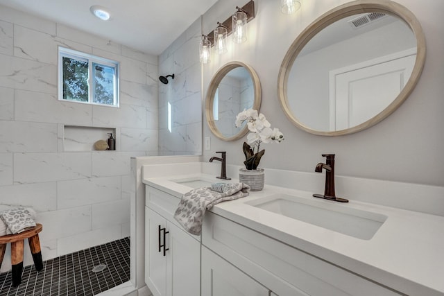 full bath featuring a sink, visible vents, tiled shower, and double vanity