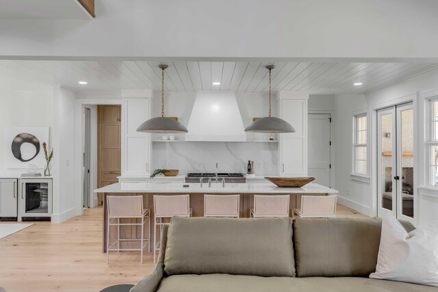 kitchen featuring beverage cooler, island range hood, decorative backsplash, light countertops, and white cabinetry