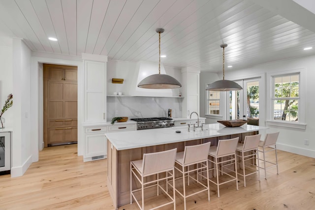 kitchen featuring a center island with sink, white cabinets, decorative backsplash, stove, and open shelves