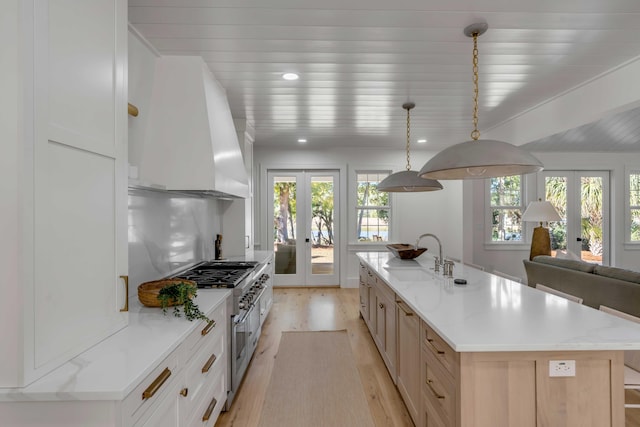 kitchen with a sink, wall chimney range hood, french doors, double oven range, and light wood finished floors