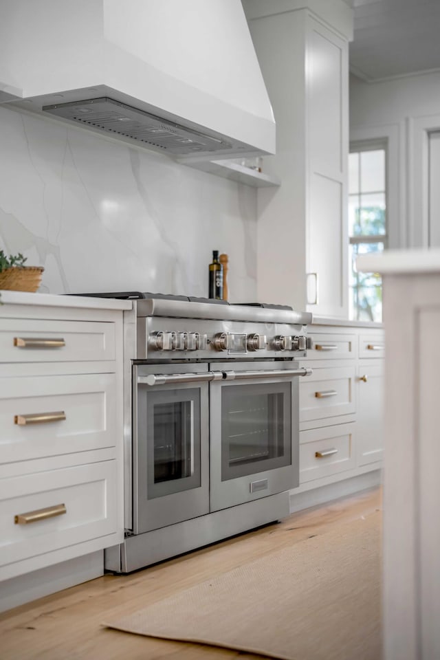 kitchen with exhaust hood, white cabinets, light countertops, light wood-type flooring, and double oven range