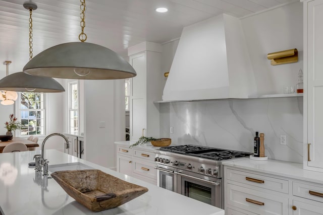 kitchen featuring range with two ovens, custom exhaust hood, tasteful backsplash, white cabinetry, and a sink