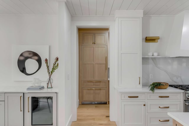 interior space with tasteful backsplash, stainless steel range, wooden ceiling, wine cooler, and light wood-type flooring