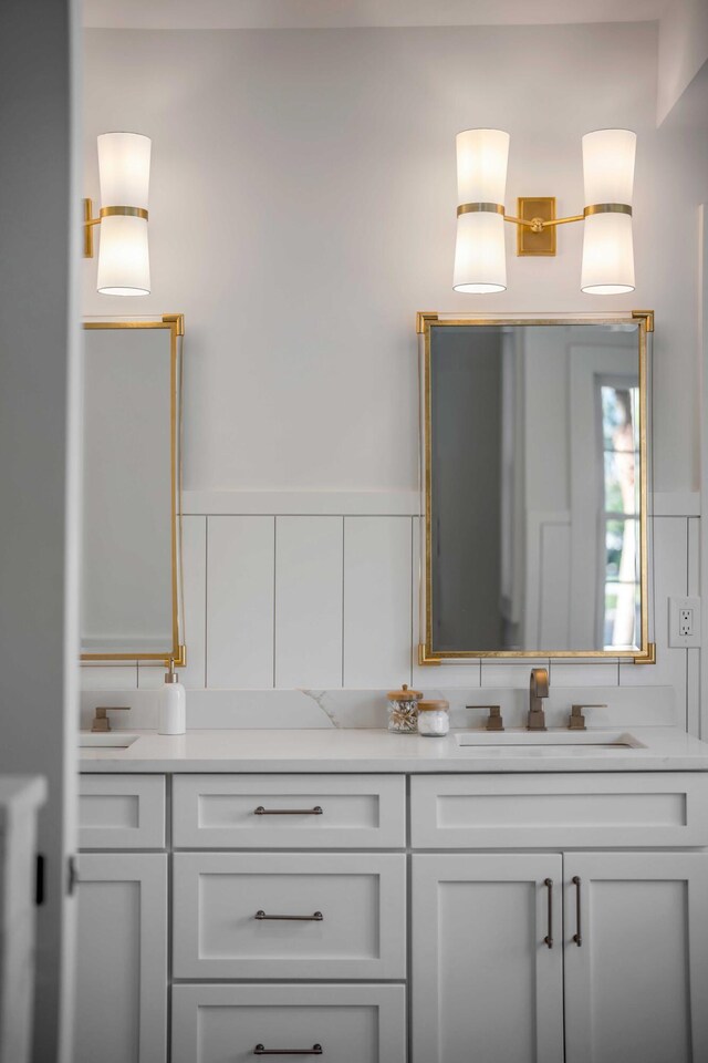 full bath featuring double vanity, a wainscoted wall, and a sink