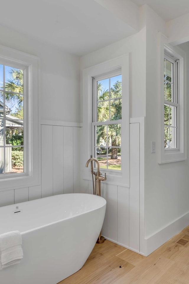 bathroom with a freestanding tub, wainscoting, visible vents, and wood finished floors