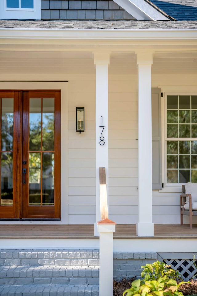 doorway to property with covered porch, french doors, and a shingled roof