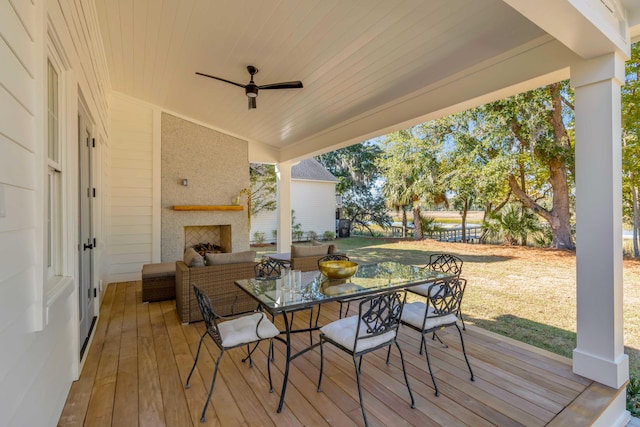 wooden deck featuring outdoor dining space, a lawn, an outdoor living space with a fireplace, and a ceiling fan