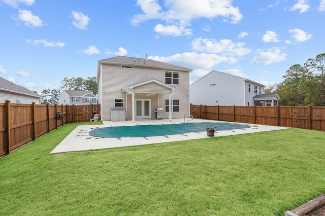 rear view of property featuring a covered pool, a patio area, and a lawn