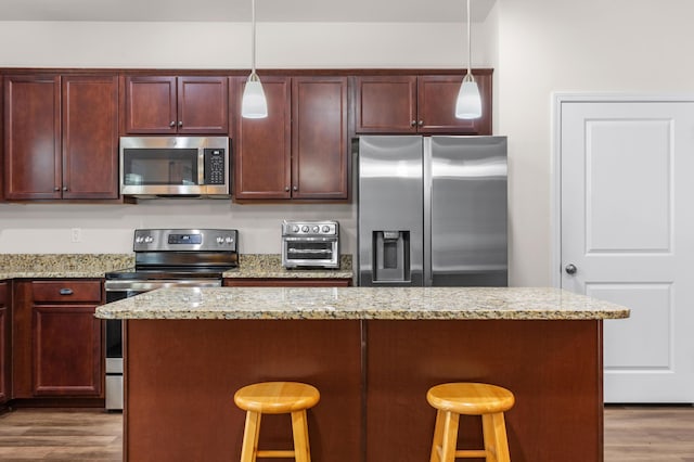 kitchen with a kitchen breakfast bar, dark hardwood / wood-style flooring, pendant lighting, and appliances with stainless steel finishes