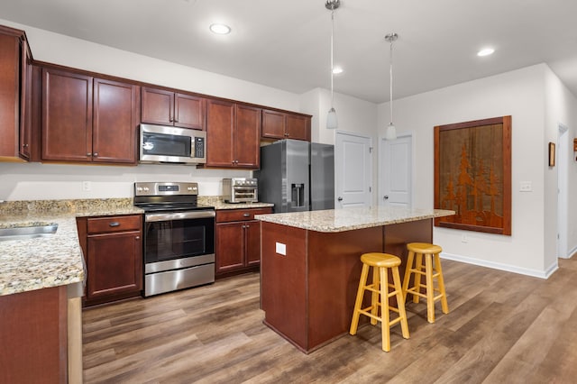 kitchen with dark wood-type flooring, a kitchen island, stainless steel appliances, and decorative light fixtures