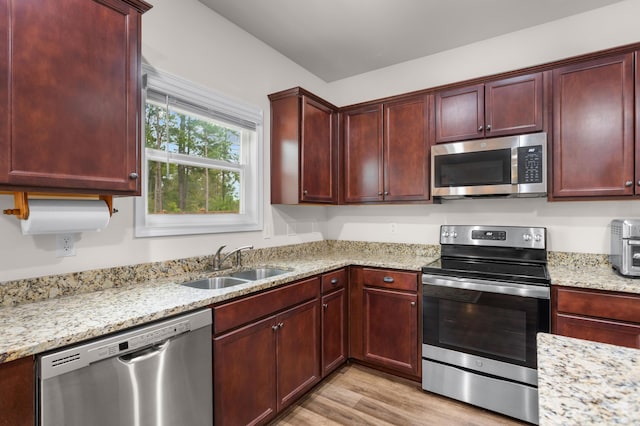 kitchen featuring stainless steel appliances, light stone counters, light hardwood / wood-style floors, and sink