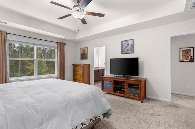 bedroom with light carpet, connected bathroom, a tray ceiling, and ceiling fan