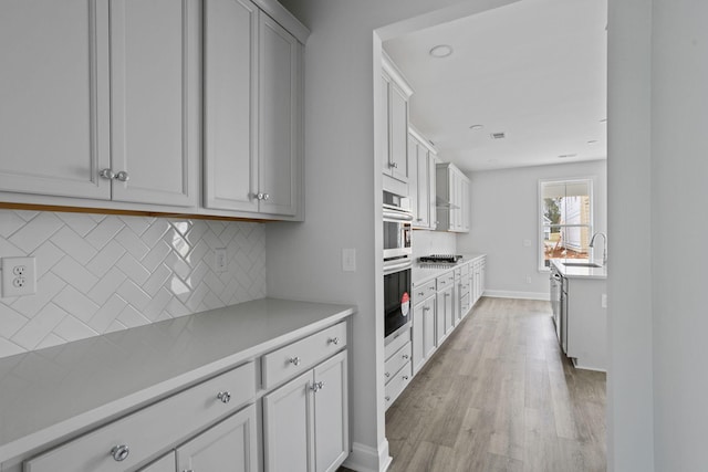 kitchen featuring tasteful backsplash, light wood finished floors, light countertops, stainless steel double oven, and a sink