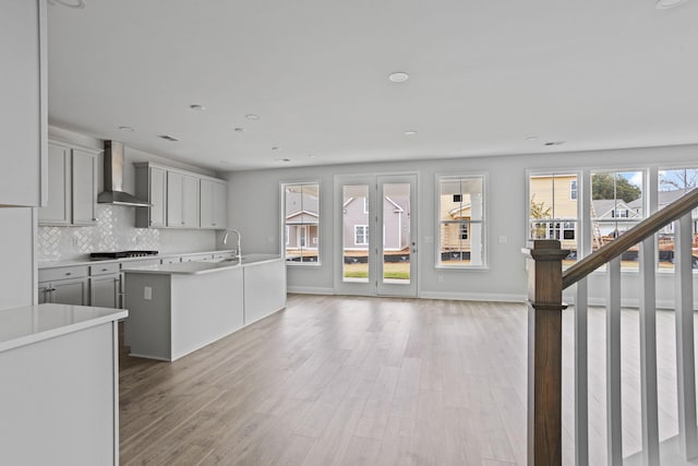 kitchen featuring light wood-type flooring, tasteful backsplash, gas stovetop, wall chimney exhaust hood, and light countertops