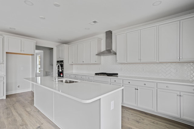 kitchen with visible vents, wall chimney range hood, light countertops, gas cooktop, and a sink