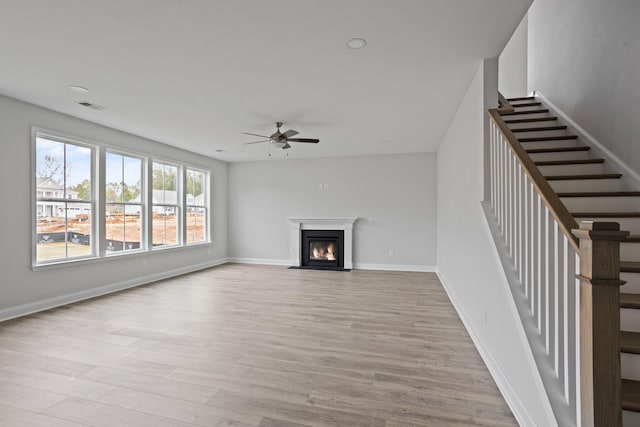 unfurnished living room featuring stairway, light wood-style flooring, a fireplace with flush hearth, and visible vents