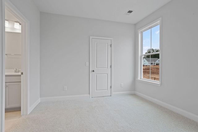 unfurnished bedroom with visible vents, light carpet, ensuite bathroom, a sink, and baseboards